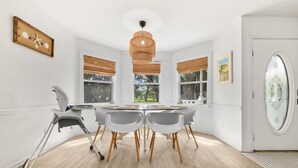 A dining area with a round table, chairs, a ceiling light, and a window with blinds. - Magnolia House- Walkable Uptown, Kids Playhouse, Peaceful Peacocks, Near Beach! (St. Augustine)