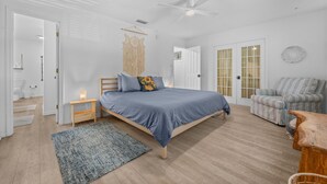 A bedroom with a bed, a chair, a ceiling fan, and a door leading to another room. - Magnolia House- Walkable Uptown, Kids Playhouse, Peaceful Peacocks, Near Beach! (St. Augustine)
