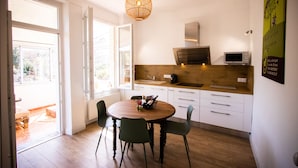 A modern kitchen with a round wooden table, two chairs, a hanging light fixture, and a microwave. - Gites Corbieres- rental with private pool, near Narbonne (Montséret)
