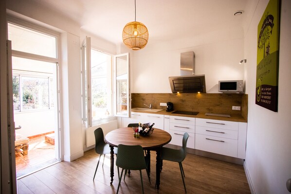 A modern kitchen with a round wooden table, two chairs, a hanging light fixture, and a microwave.