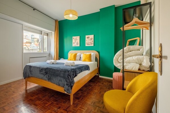 A bedroom with a bed, a chair, a hanging light, and a mirror. - GuestReady - Back to Little World (Porto)