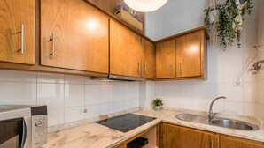 A kitchen with wooden cabinets, a built-in microwave, a stovetop, and a sink. - GuestReady - Miragaia Green (Porto)