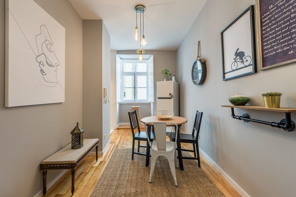 A cozy dining area with a round table, chairs, and a rug. A clock and framed artwork adorn the walls. - GuestReady - Miragaia Green (Porto)