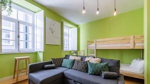 A modern living room with a grey sectional sofa, a wooden bunk bed, and a green wall. - GuestReady - Miragaia Green (Porto)