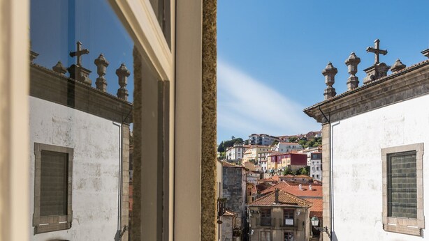 A view of a narrow street with buildings on either side, featuring traditional architecture with balconies and decorative elements. - GuestReady - Miragaia Green (Porto)