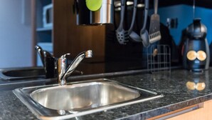 Una cocina con un lavamanos de acero inoxidable, una encimera negra y varios utensilios colgando sobre él.