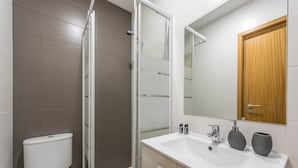Un baño moderno con inodoro, ducha, lavamanos y espejo.