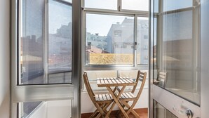 Un balcone con tavolo e sedie in legno, vista su edifici e una porta con maniglia.
