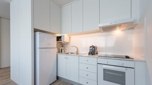 Cozinha compacta com armários brancos, forno embutido, micro-ondas e cafeteira.