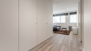Quarto moderno e minimalista com um guarda-roupa grande, um sofá cinzento e uma pequena mesa.