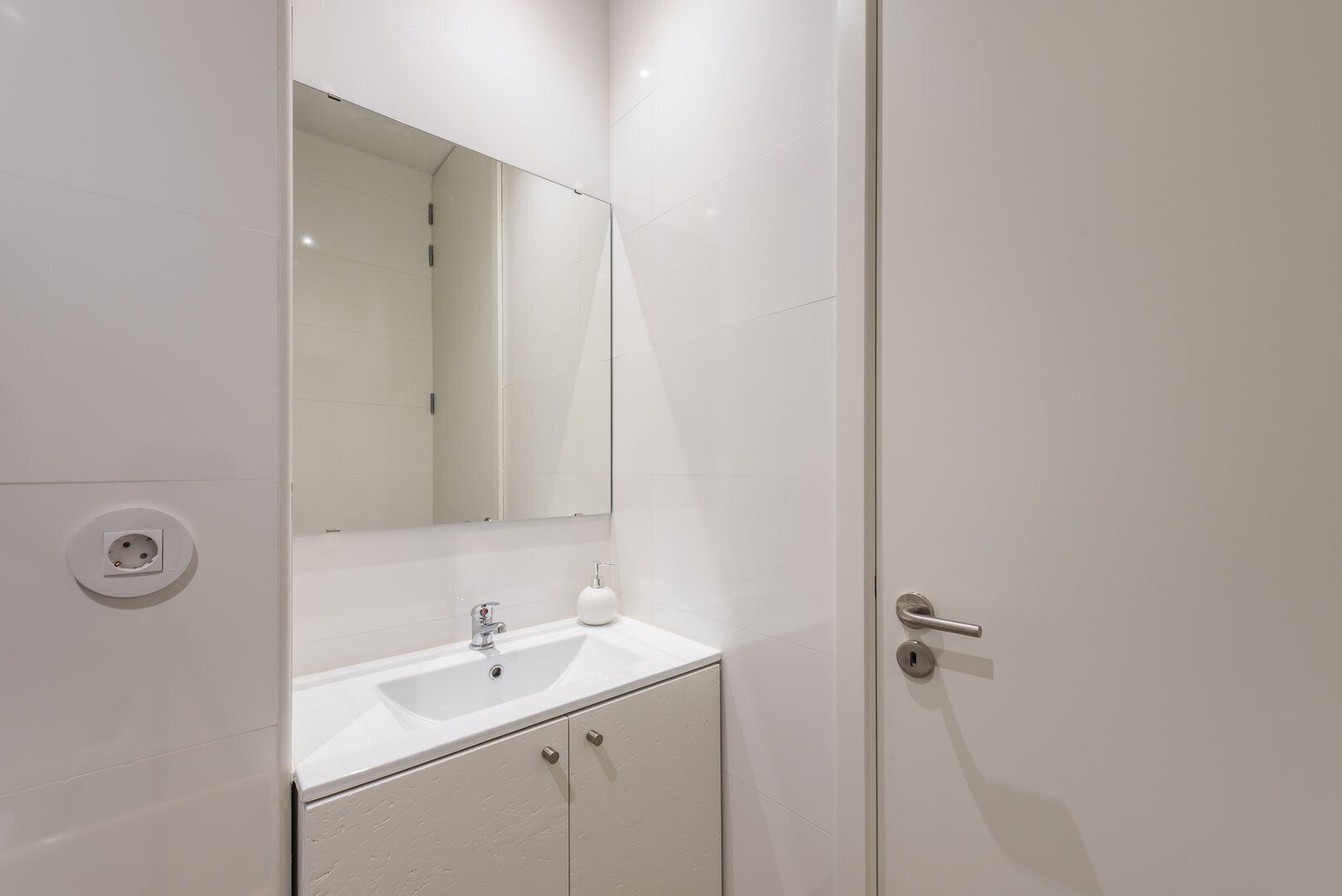 A modern bathroom with a white sink, a mirror, and a door.