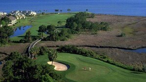 Vista aérea de um campo de golfe com um corpo d'água, árvores e uma vista distante do oceano.
