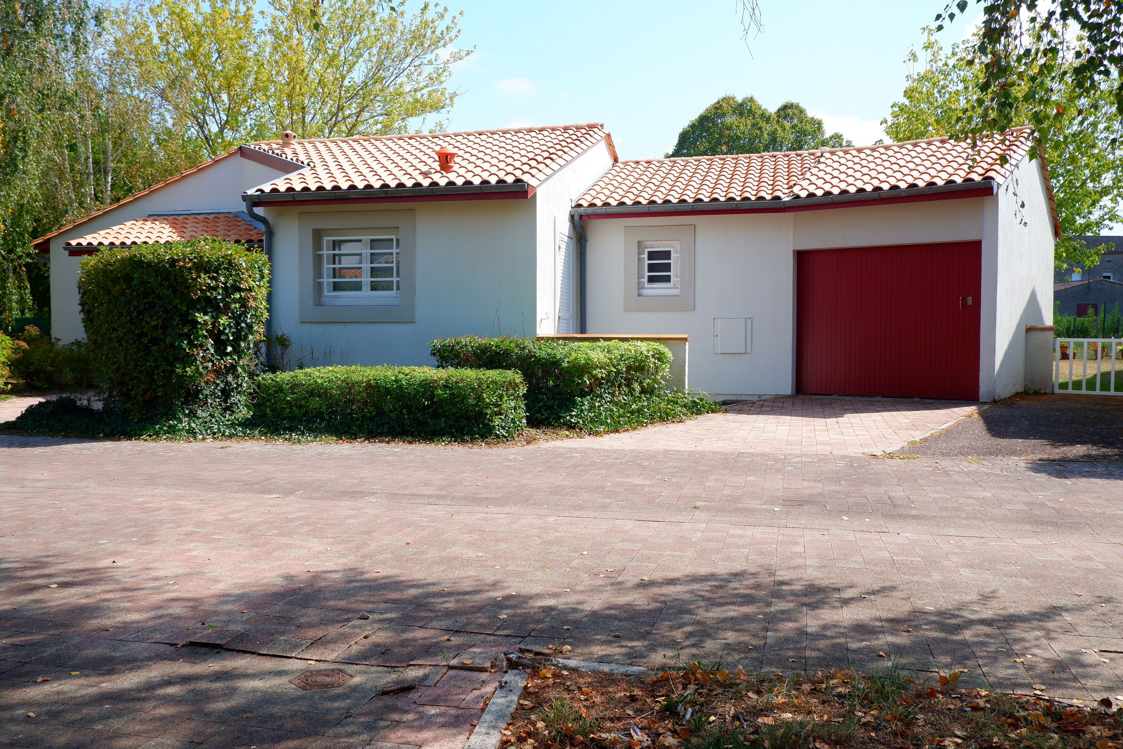 Una casa de un solo piso con techo de tejas rojas, puerta de garaje roja y entrada pavimentada.