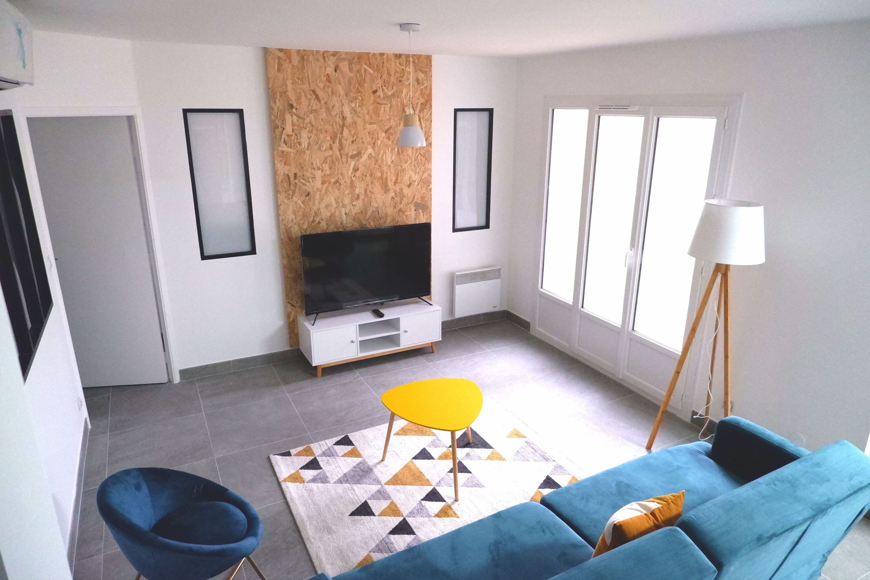 A living room with a blue sofa, a yellow chair, a TV, and a lamp.