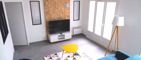 A living room with a blue sofa, a yellow chair, a TV, and a lamp.