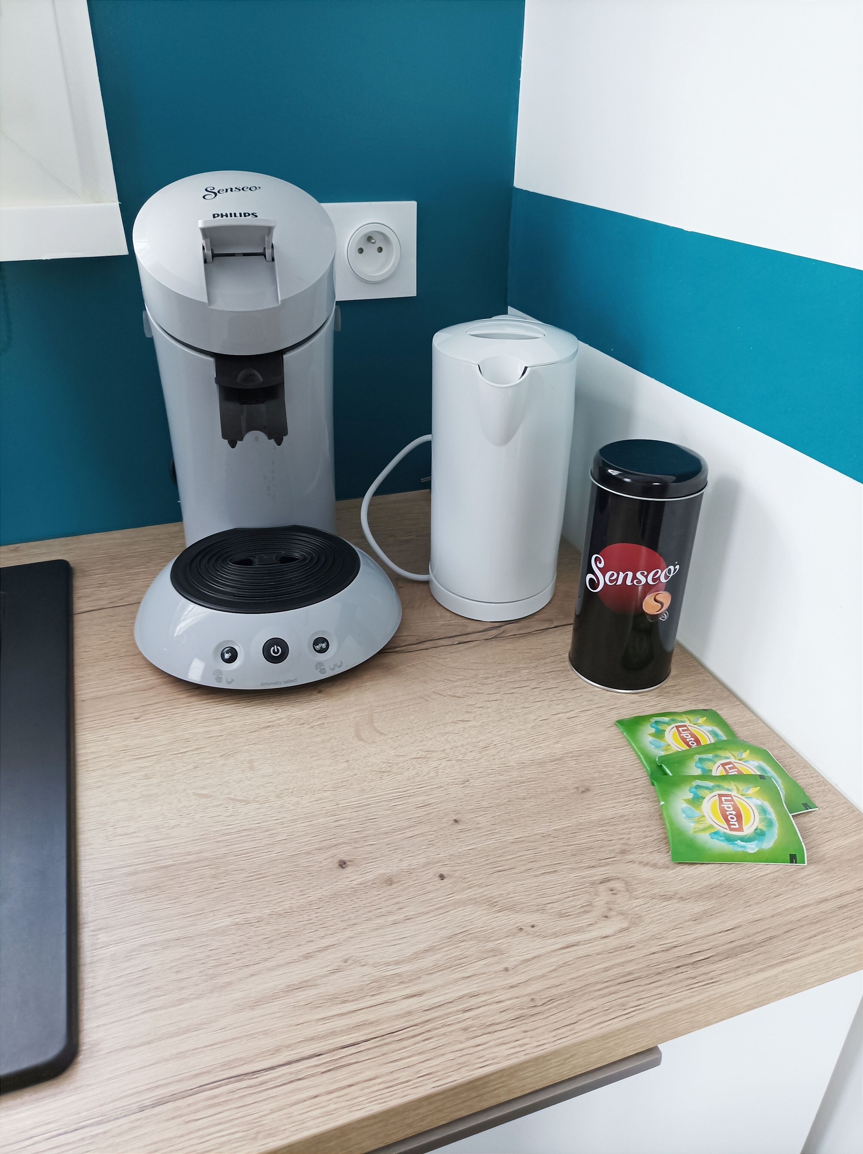 Une machine à café, un appareil cylindrique blanc, et une tasse noire posée sur une surface en bois.