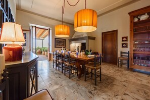 Un espace repas doté d’un sol en marbre, d’une table en bois, de chaises, de lampes suspendues et d’un meuble contenant de la verrerie.