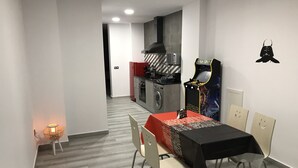 Een moderne eetruimte met een tafel gedekt voor twee personen, een keuken op de achtergrond, en een Star Wars speelautomaat.