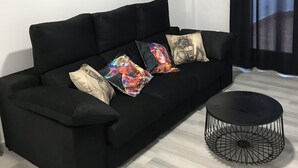 Een zwarte bank met kleurrijke kussens, een ronde zwarte salontafel en een plafondairconditioner.
