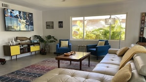 Una sala de estar moderna con un sofá color beige, sillones azules, una mesa de centro y un televisor en la pared.