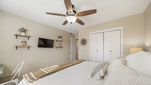 A bedroom with a bed, a ceiling fan, a TV, and a wardrobe.