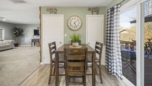 A dining area with a wooden table, four chairs, a potted plant, and a wall clock.