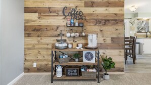 A coffee bar setup with a wooden backdrop, a coffee machine, mugs, and a sign that reads "Sip & Repeat".