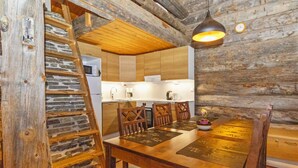 Un interior rústico de madera con una mesa de comedor, sillas y una zona de cocina con armarios de madera y una pared de piedra.