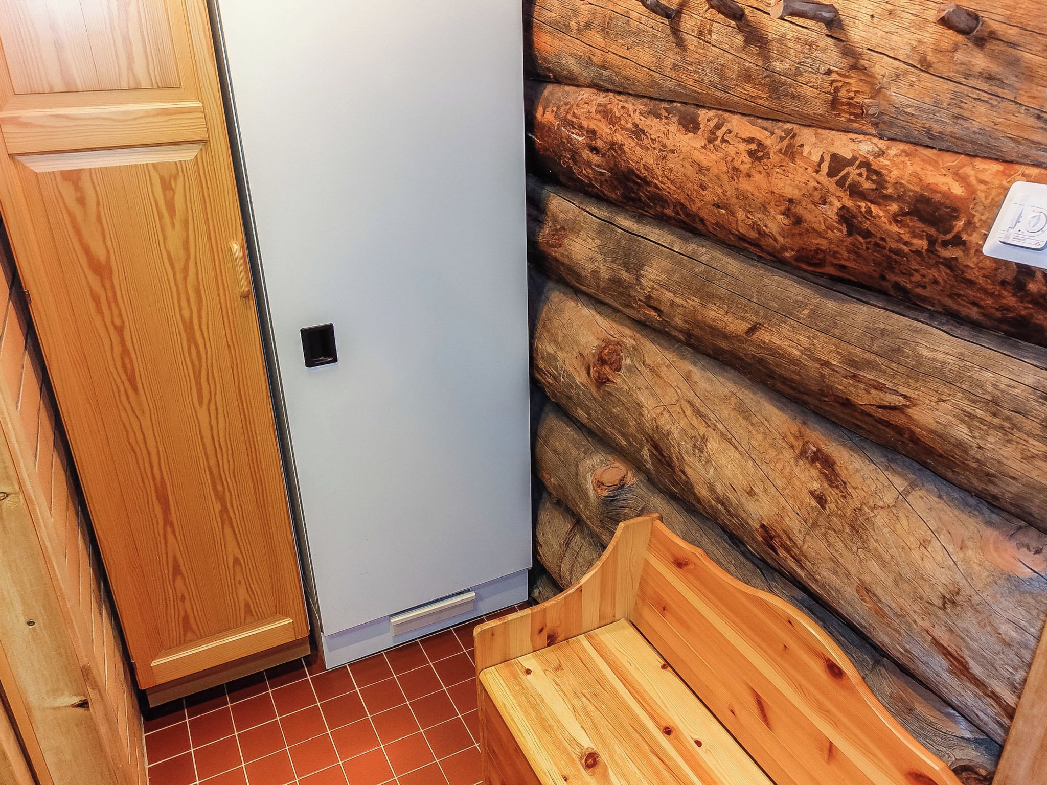 A corner of a room with a wooden cabinet, a white door, and a log wall.