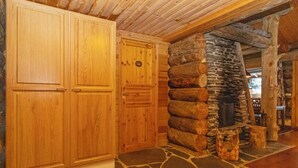 Interior de una cabaña de troncos con paredes de madera, una chimenea de piedra y piso de baldosas.