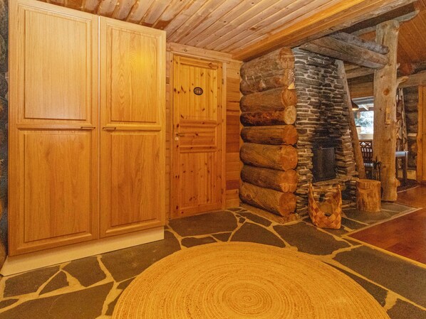 A log cabin interior with wooden walls, a stone fireplace, and a tiled floor.