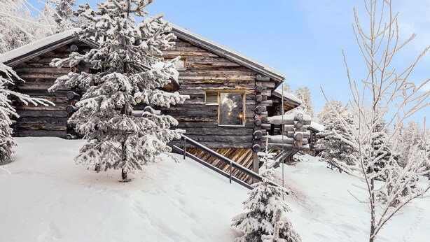 Una cabaña de troncos con fachada de madera, rodeada de árboles cubiertos de nieve.