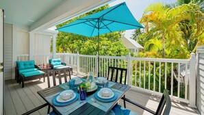 A covered outdoor deck with a table set for dining, surrounded by white railings and lush greenery. - **SERENITY ON SOUTHARD @ THE ANNEX** Condo + Last Key White Glove Service... (Key West)