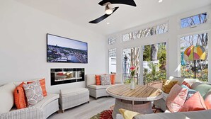 Amplia sala de estar con televisor grande, mobiliario de mimbre y vistas al exterior.