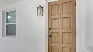 A white exterior wall with a wooden door, a window, and a wall-mounted light fixture.