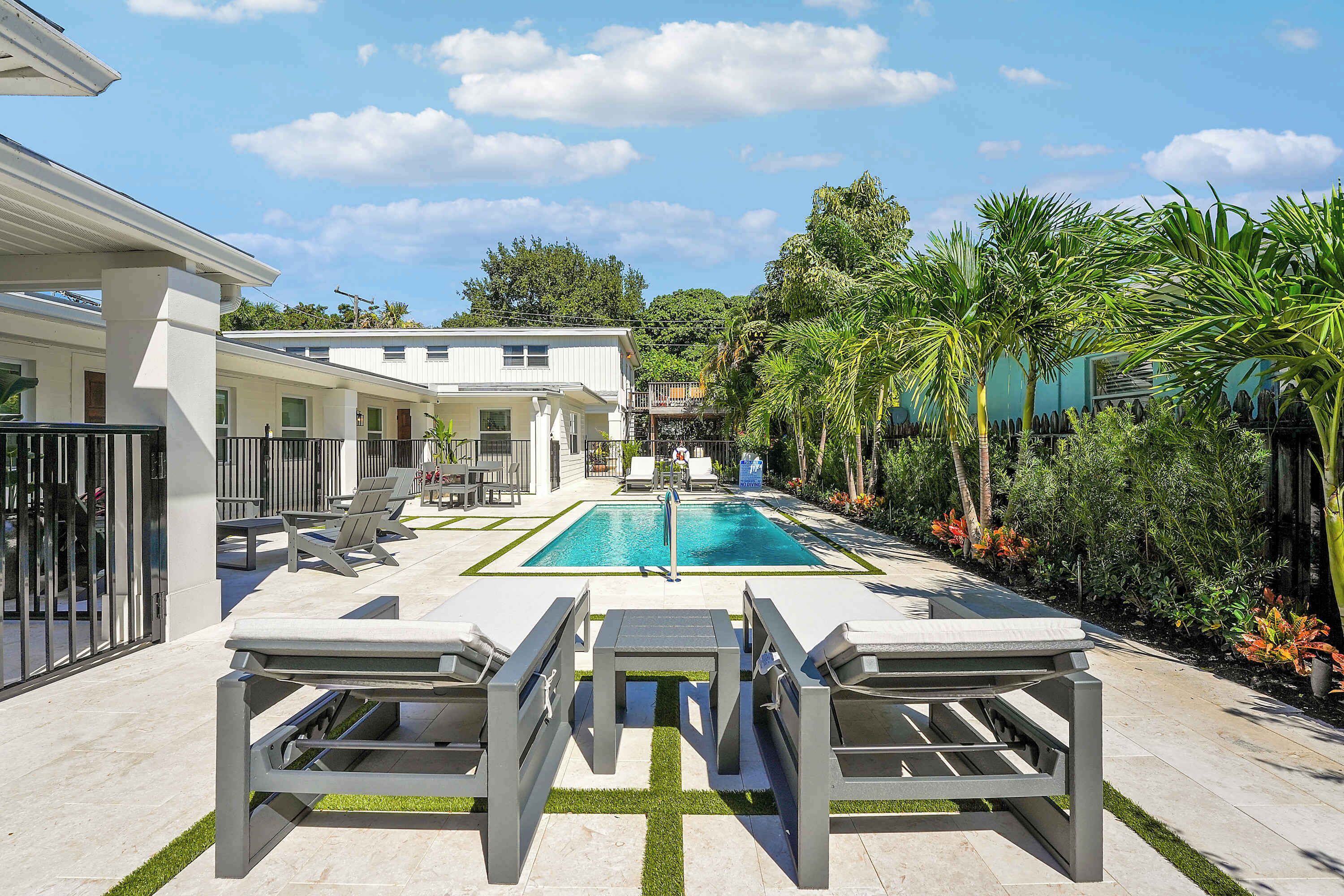 A pool area with lounge chairs and a table, surrounded by greenery and a building with multiple balconies.