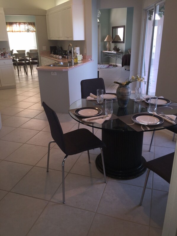 Une cuisine moderne avec des meubles blancs, un coin repas doté d’une table en verre et une vue sur le salon.