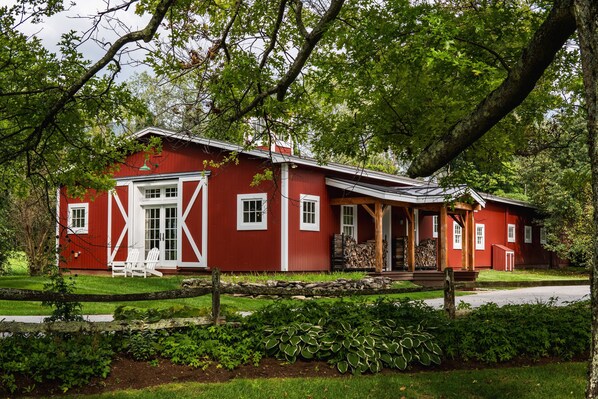 Una casa de estilo granero roja con un porche y una cerca de piedra.