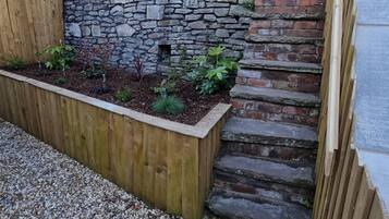 Un bac à fleurs en bois contenant diverses plantes, un mur en pierre et un escalier en briques.