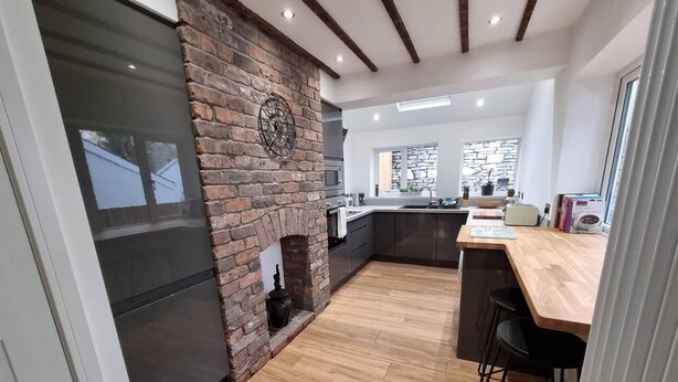 A modern kitchen with a brick wall, wooden flooring, and a large refrigerator.