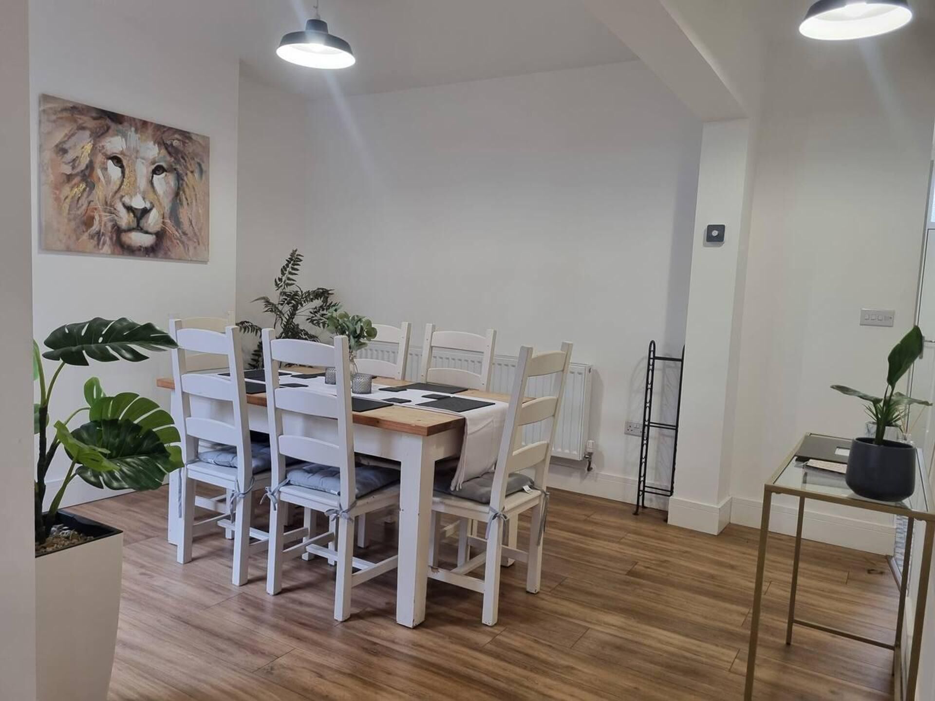 A dining area with a white table and chairs, a painting of a lion, and a potted plant.
