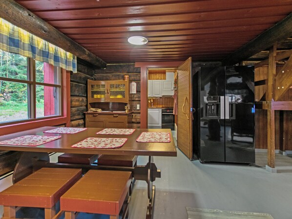 L’intérieur d’une cabane comprend une table à manger en bois, des bancs, un coin cuisine et un réfrigérateur.
