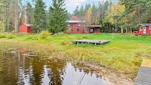 Un chalet au bord du lac, doté d’un quai, entouré d’une forêt dense et d’un petit étang.