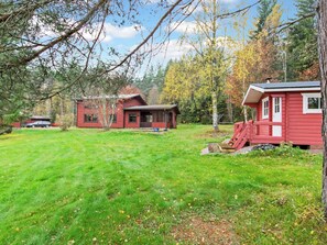 A red cabin with a porch, surrounded by a grassy yard and trees.