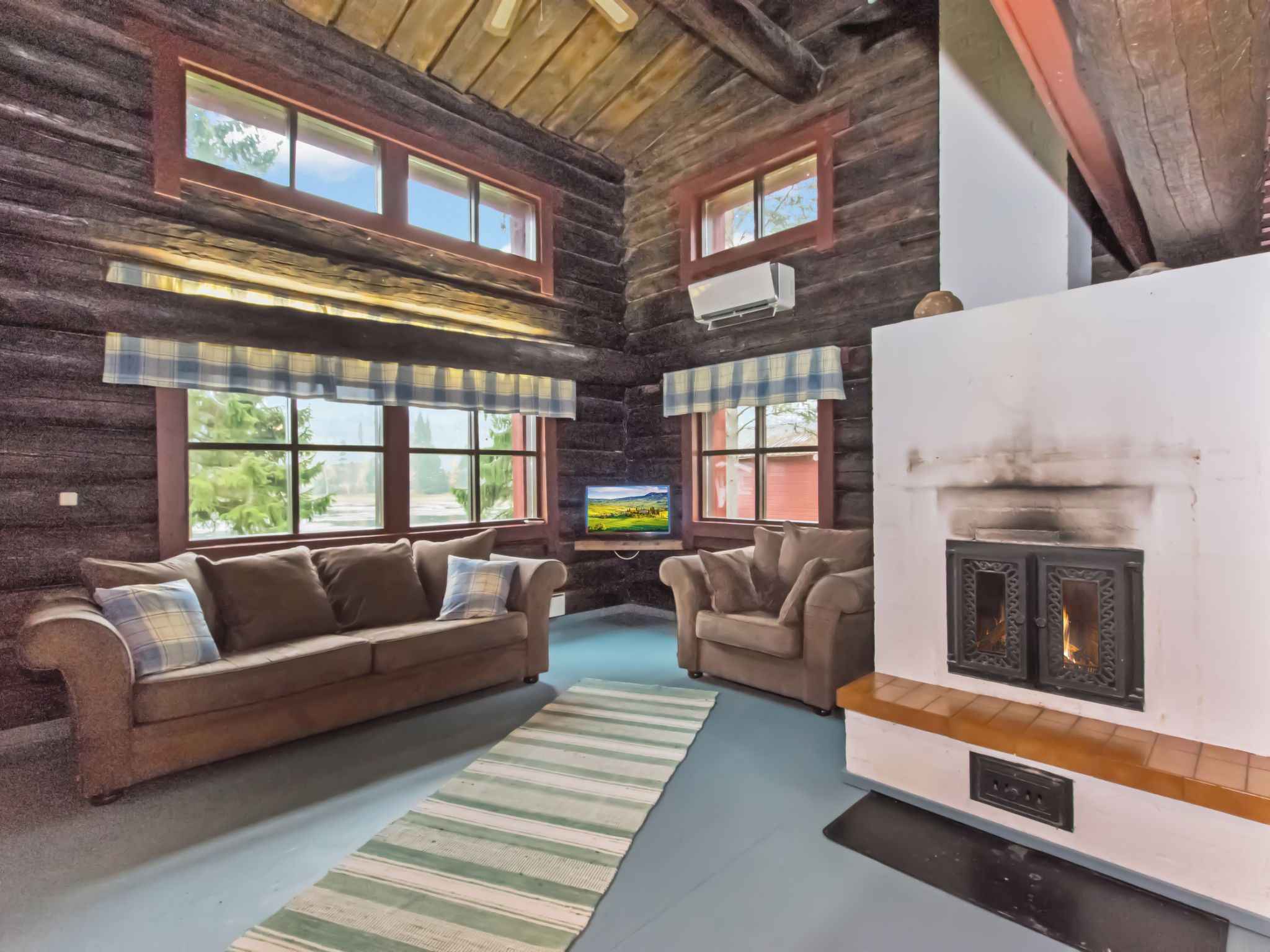 Ein rustikaler Innenraum einer Blockhütte mit zwei Sofas, einem Kamin und großen Fenstern.