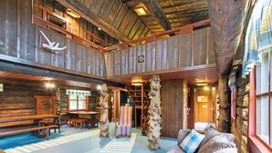 L’intérieur d’un chalet rustique comprend un coin repas en bois, un canapé avec des coussins à carreaux et une grande sculpture représentant un tronc d’arbre.