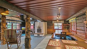 L’intérieur d’un chalet rustique est agrémenté d’un plafond en bois, d’une cheminée, d’un coin repas avec des bancs et d’un salon avec un canapé et un fauteuil à bascule.