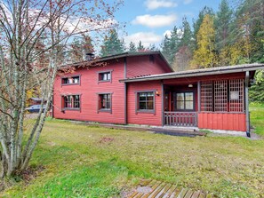 Een rode houten woning met een veranda en een omheind terrein.