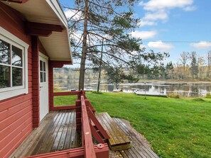A wooden deck with a red railing, a grassy lawn, and a view of a lake with reflections. - Kurelahti by Interhome (Petäjävesi)