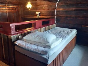 A wooden room with a bed, a red bench, and a wall-mounted light fixture.